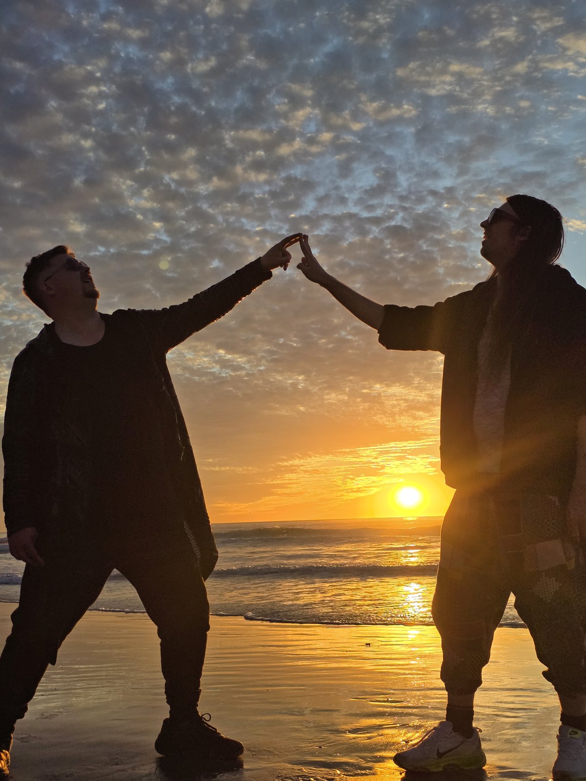 Two silhouettes touching outstretched fingers above the setting sun on a beach